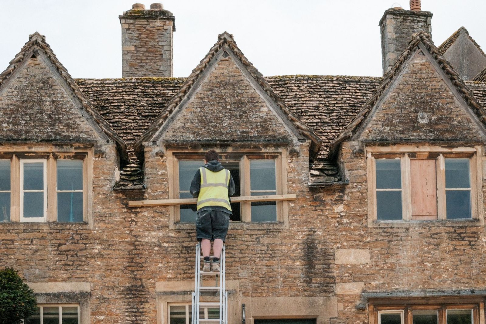 Handwerker auf der Leiter arbeitet an der Fassade eines Steinhauses