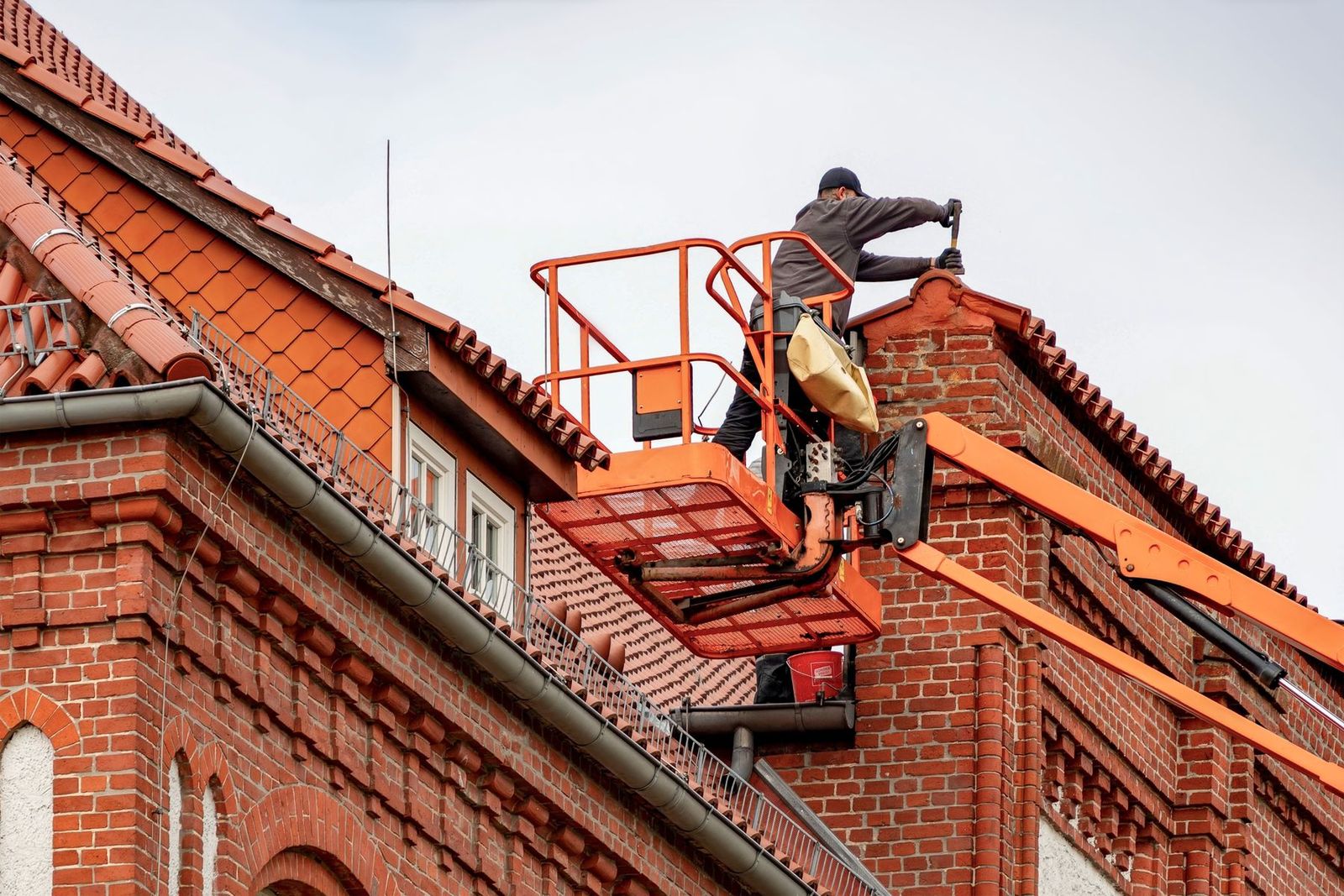 Monteur im Hubsteiger arbeitet an der Traufe eines Backsteinhauses mit Ziegeldach